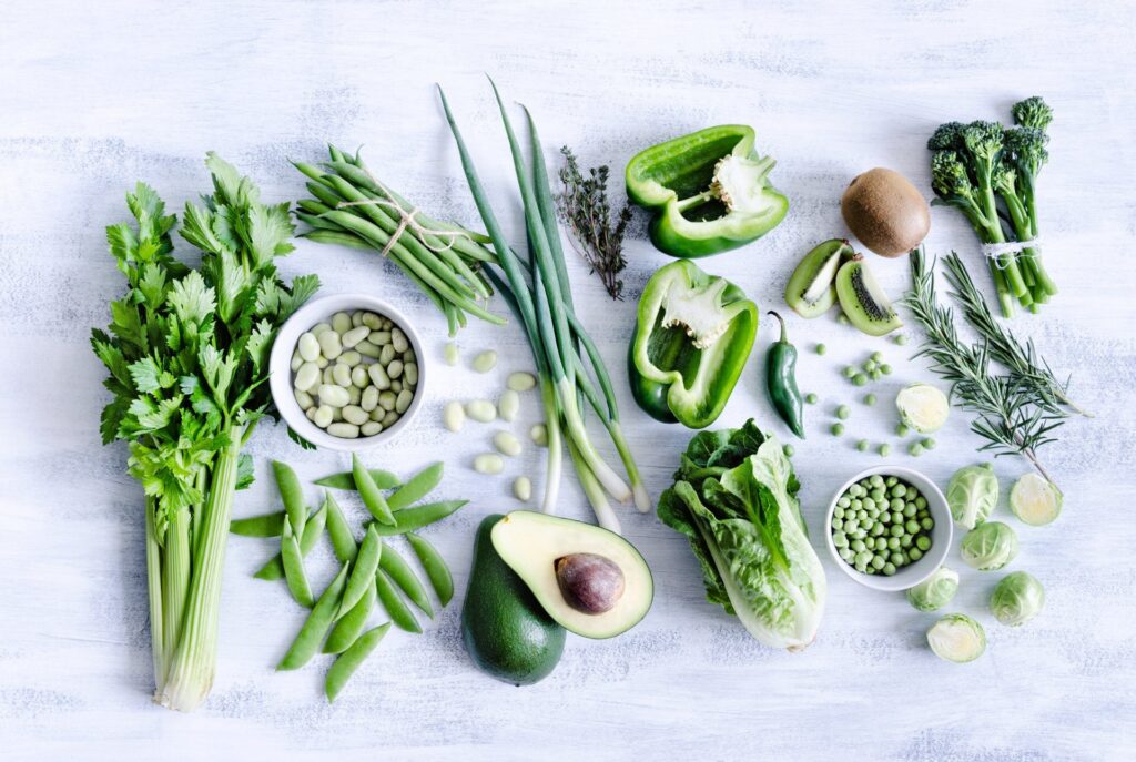 Groene groente van bovenaf op een witte tafel: selderij, peultjes, avocado, paprika en doperwten