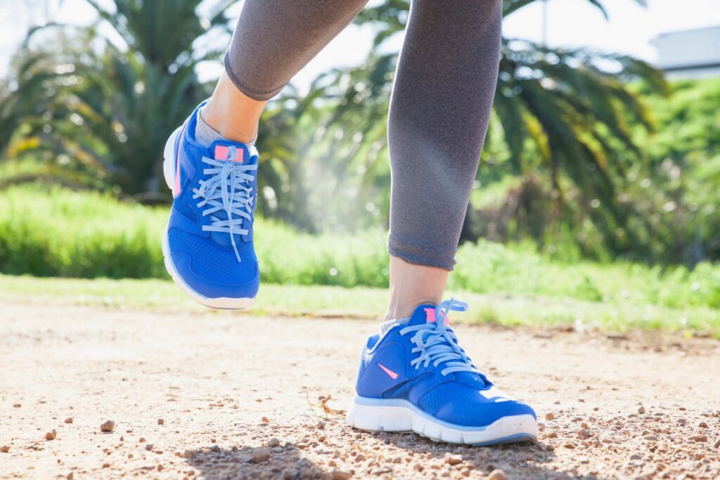 Benen van een hardloper in blauwe schoenen op een zandpad